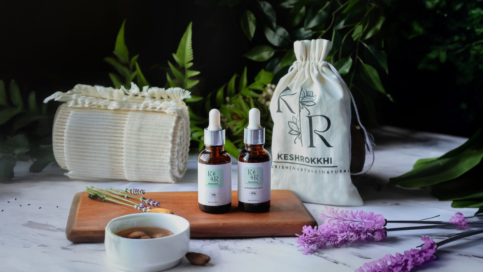 Keshrokkhi Hriddhi Superserum and Shondhi hair serum displayed with pouch, towel, and herbs- premium organic haircare brand from Dhaka, Bangladesh