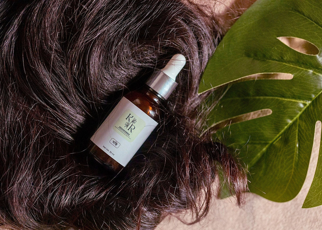 Shondhi natural hair serum by Keshrokkhi placed on wavy black hair with a tropical leaf, symbolizing shine and nourishment