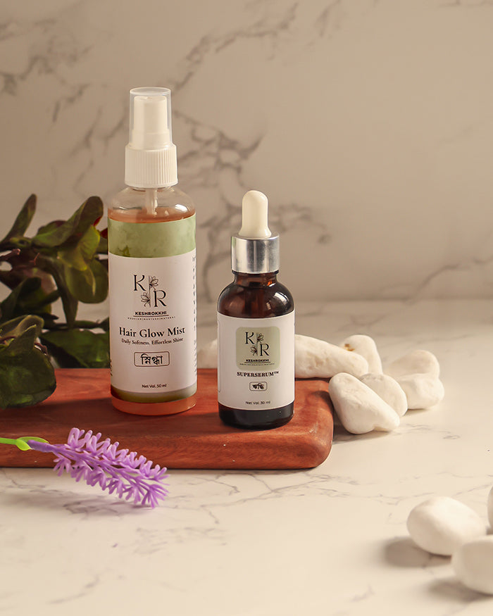 Two haircare products on a wooden tray with a plant and lavender flower in the background. Bangladesh's best Anti Hair Fall, Pro Hair Growth and Shine Combo.