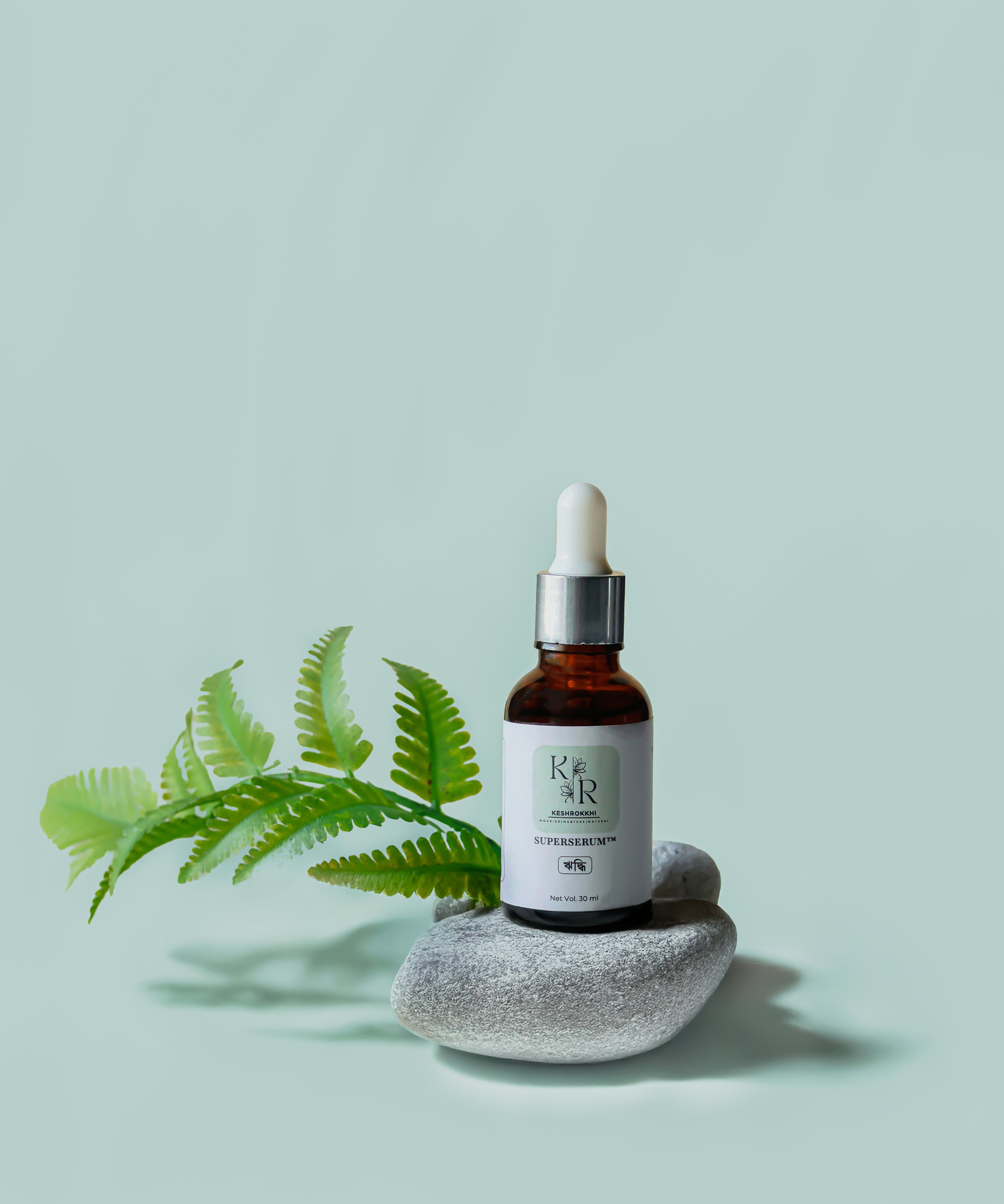 Hriddhi SuperSerum hair serum by Keshrokkhi placed on spa stones with green fren on soft pastel background